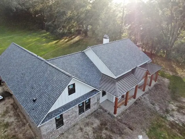 Dark shingle roof and white standing-seam porch roof on a new home, drone view in low sun.