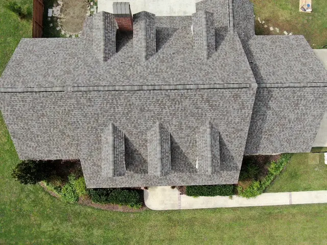 Grey shingle roof with three tall dormers on a white two-storey home.