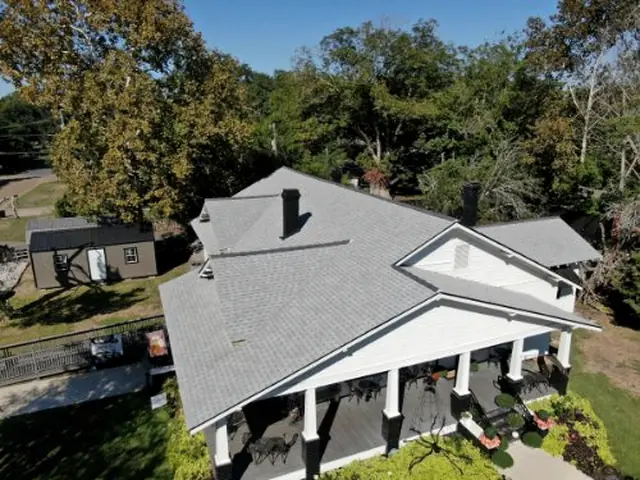 Grey shingle roof on a white columned porch home under mature trees.
