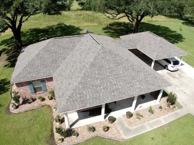 Completed shingle roof on a brick ranch home with an attached carport, under live oaks.