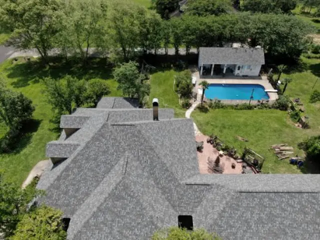 Grey shingle roof on a home with a swimming pool and pool house behind it.